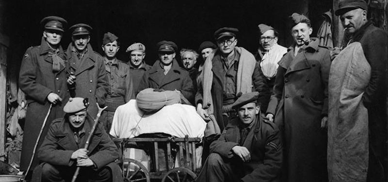 A group of British prisoners of war in winter great coats pose around a civilian-made cart after being released from captivity.